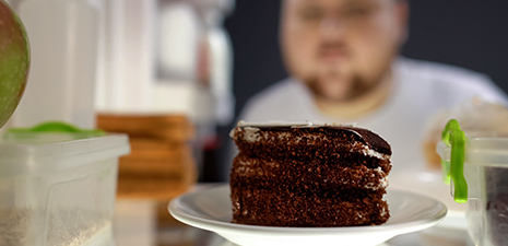a man looking at a piece of chocolate cake in a refrigerator
